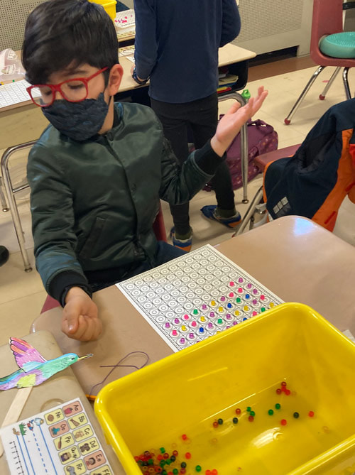 PS118 student makes a 100th day necklace in class.