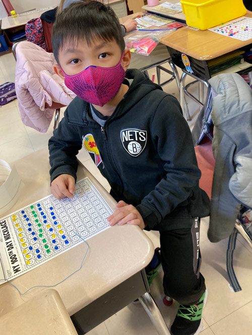 Elementary student makes a 100th day necklace in class.
